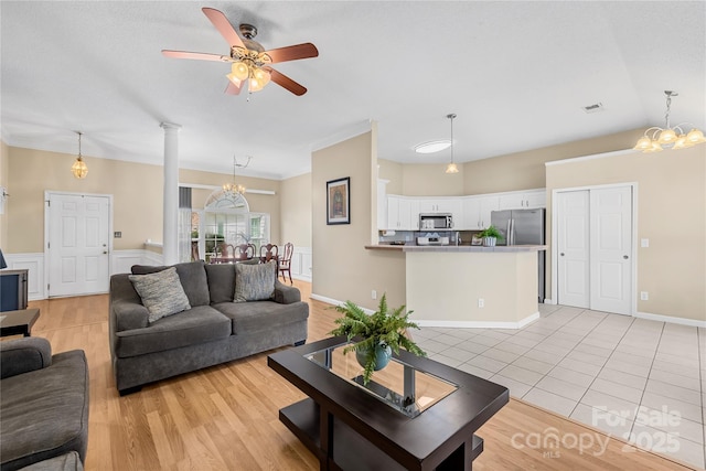 living area with visible vents, light wood-type flooring, decorative columns, wainscoting, and ceiling fan with notable chandelier