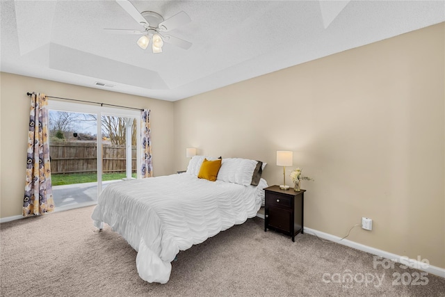 bedroom with a tray ceiling, carpet floors, baseboards, and access to outside