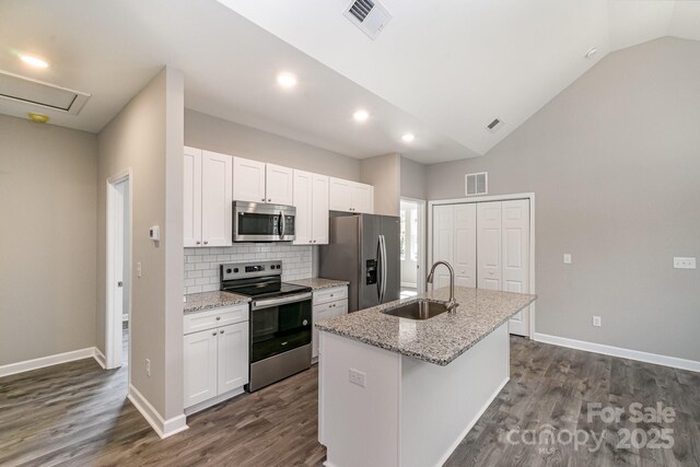 kitchen featuring a kitchen island with sink, a sink, appliances with stainless steel finishes, white cabinets, and vaulted ceiling