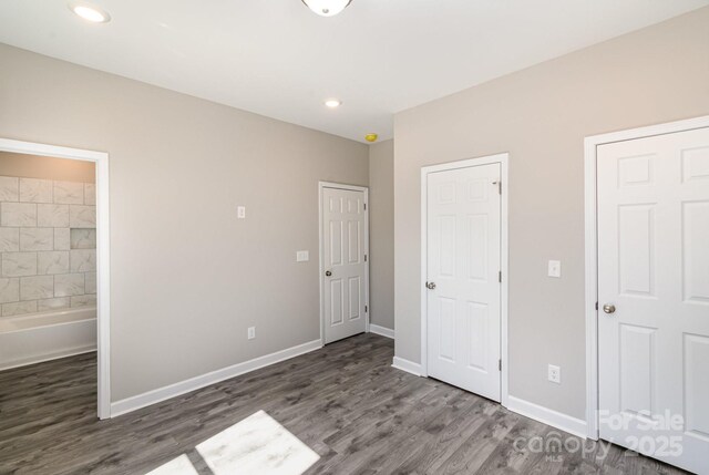 unfurnished bedroom featuring recessed lighting, ensuite bathroom, baseboards, and wood finished floors