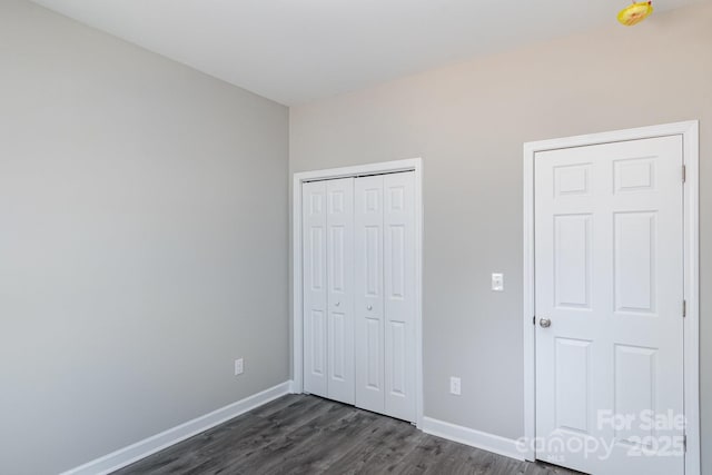 unfurnished bedroom with a closet, baseboards, and dark wood-type flooring