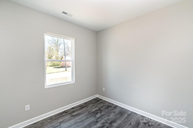 spare room featuring dark wood-style floors, visible vents, and baseboards