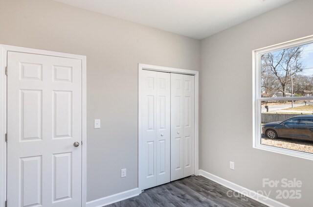 unfurnished bedroom featuring dark wood finished floors, a closet, and baseboards