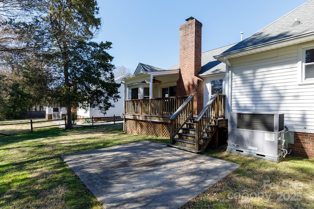 rear view of property with fence, a chimney, a deck, a yard, and a patio area