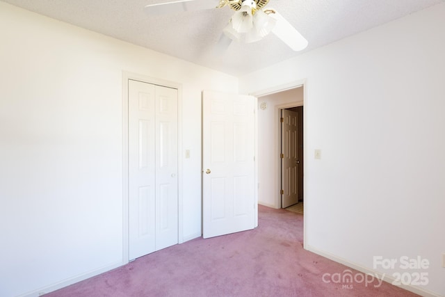 unfurnished bedroom with baseboards, ceiling fan, light colored carpet, a closet, and a textured ceiling