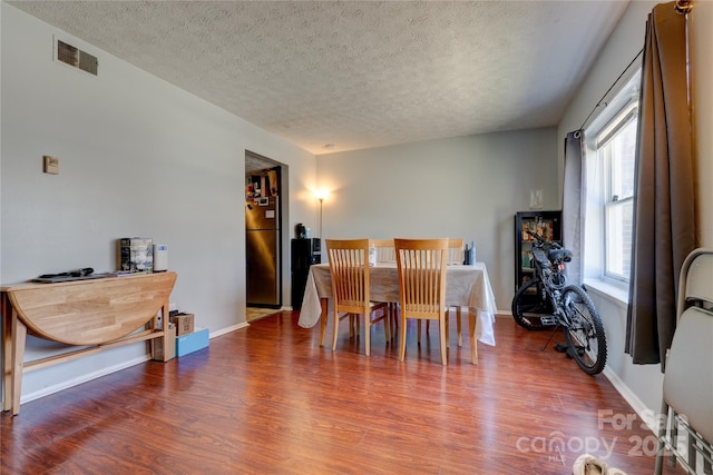 dining space featuring visible vents, a textured ceiling, baseboards, and wood finished floors