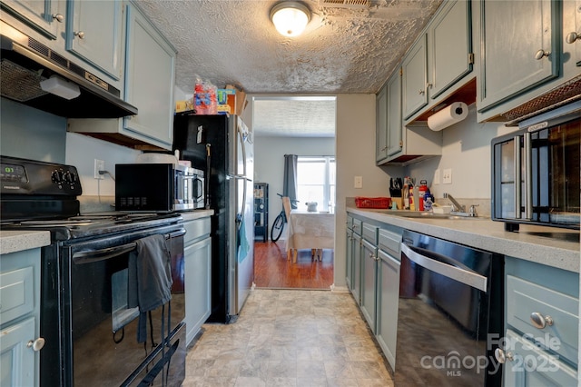 kitchen with under cabinet range hood, a sink, a textured ceiling, appliances with stainless steel finishes, and light countertops