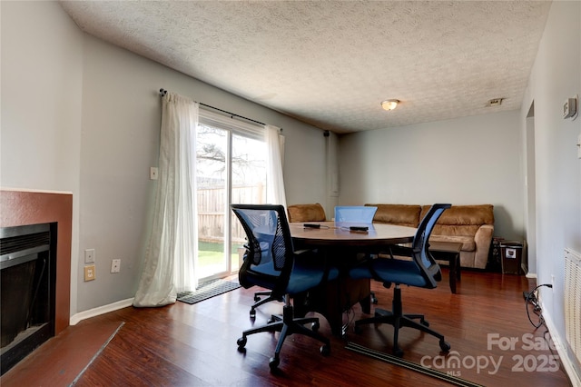 office space featuring baseboards, a textured ceiling, wood finished floors, and a fireplace