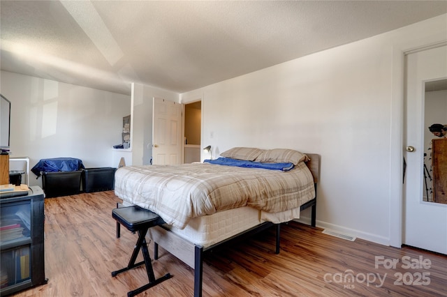 bedroom with visible vents, light wood-style flooring, a textured ceiling, and baseboards