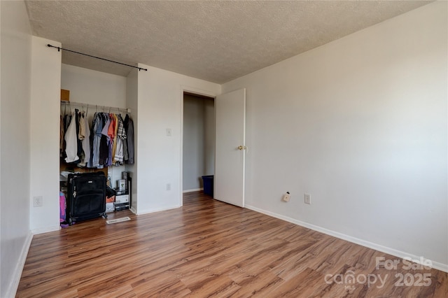 unfurnished bedroom featuring a closet, baseboards, a textured ceiling, and wood finished floors