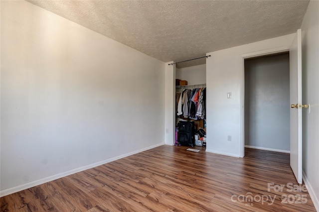 unfurnished bedroom featuring a closet, a textured ceiling, baseboards, and wood finished floors