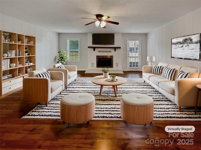 living area featuring ceiling fan, plenty of natural light, a brick fireplace, and wood finished floors