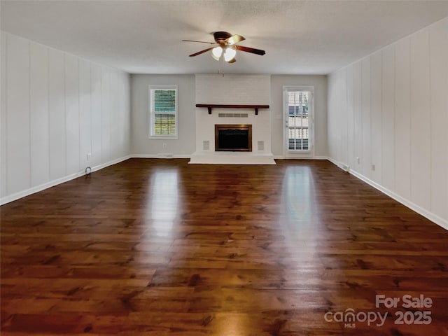 unfurnished living room featuring a brick fireplace, dark wood finished floors, a ceiling fan, and a healthy amount of sunlight