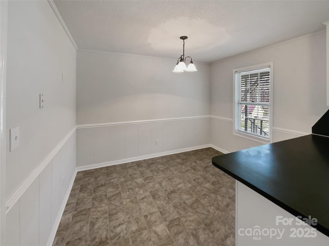 unfurnished dining area with a wainscoted wall, a textured ceiling, and an inviting chandelier