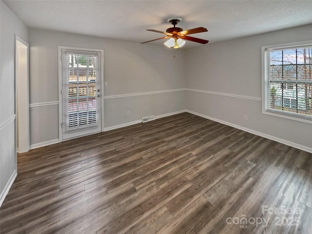 unfurnished room featuring dark wood-type flooring, visible vents, and a wealth of natural light