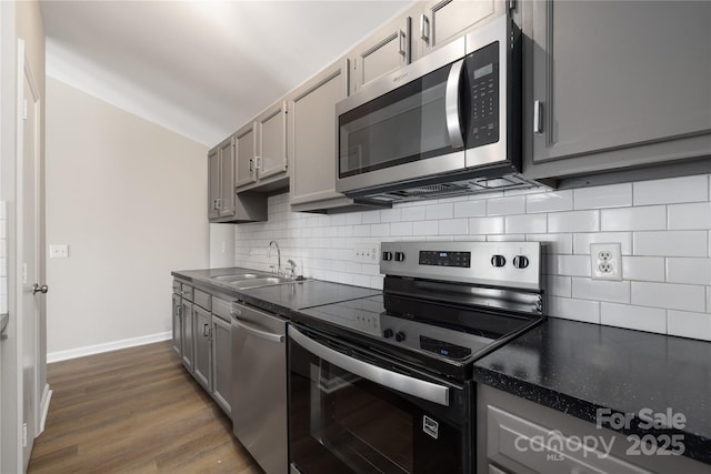 kitchen with a sink, stainless steel appliances, dark countertops, and gray cabinets