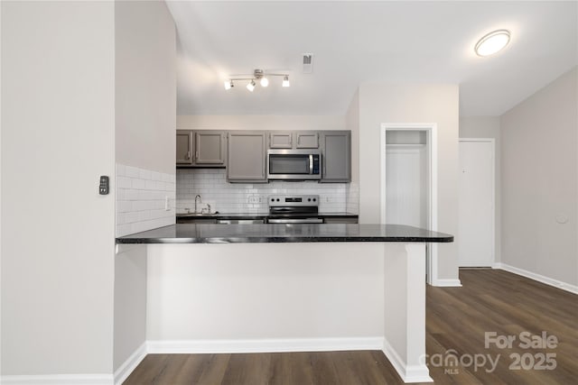 kitchen with a peninsula, gray cabinets, dark wood-style flooring, stainless steel appliances, and tasteful backsplash