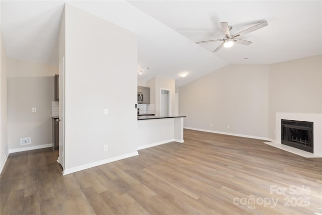 unfurnished living room with lofted ceiling, a fireplace with flush hearth, wood finished floors, and ceiling fan