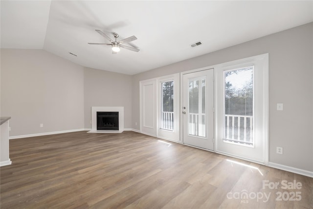 unfurnished living room with visible vents, baseboards, ceiling fan, a fireplace with flush hearth, and wood finished floors