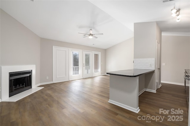 unfurnished living room featuring vaulted ceiling, a fireplace with raised hearth, and dark wood-style flooring