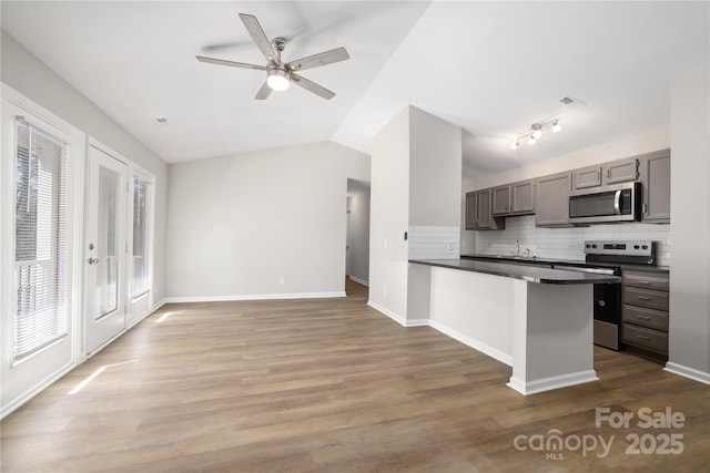 kitchen with gray cabinetry, dark countertops, wood finished floors, stainless steel appliances, and lofted ceiling