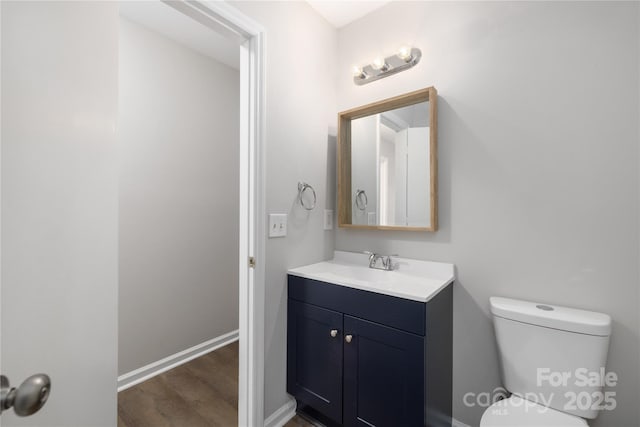 half bathroom featuring baseboards, toilet, wood finished floors, and vanity