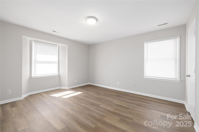 unfurnished room featuring visible vents, wood finished floors, and baseboards