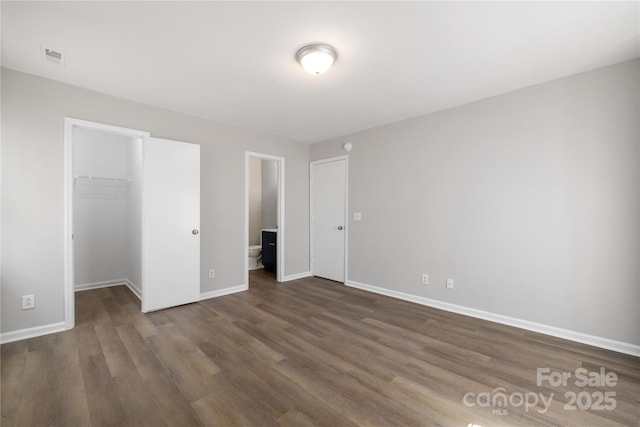 unfurnished bedroom featuring a closet, baseboards, dark wood-style flooring, and a spacious closet