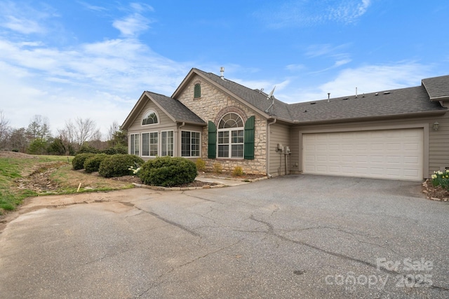 view of front of home with an attached garage, stone siding, driveway, and roof with shingles