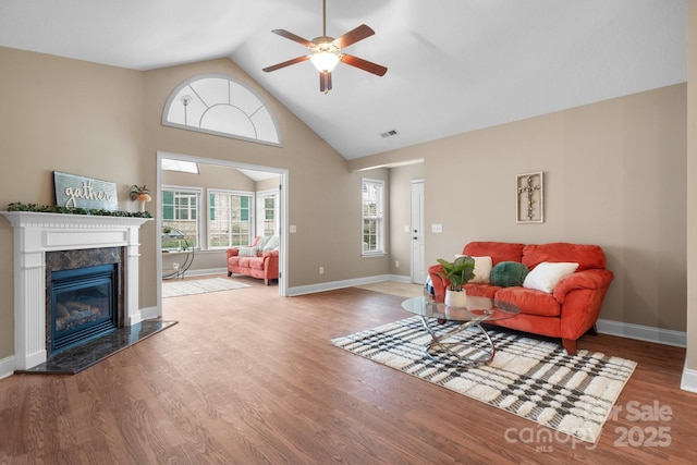living room with a high end fireplace, wood finished floors, high vaulted ceiling, visible vents, and a ceiling fan