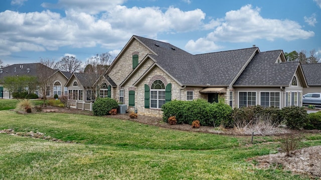 view of front of house with central air condition unit, stone siding, a shingled roof, and a front lawn