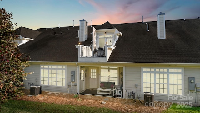 rear view of house with a balcony, roof with shingles, and a chimney