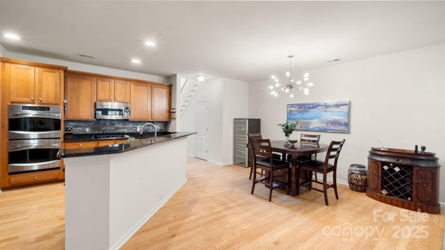 kitchen with light wood-type flooring, tasteful backsplash, a chandelier, and stainless steel appliances