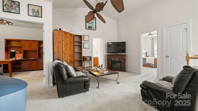 living room with high vaulted ceiling, light colored carpet, a stone fireplace, and a ceiling fan