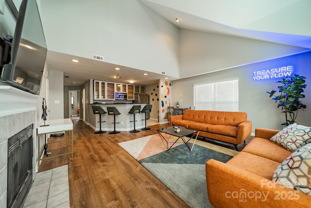 513 N Graham St Unit 3H, Charlotte, NC 28202 - living room featuring high vaulted ceiling, light wood-style flooring, visible vents, a tiled fireplace, and baseboards