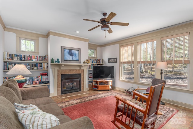 living room featuring a ceiling fan, crown molding, a fireplace, and baseboards