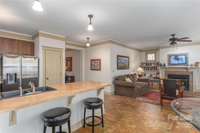 kitchen with a fireplace, a sink, light countertops, stainless steel refrigerator with ice dispenser, and a kitchen bar