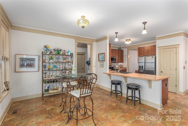 kitchen featuring appliances with stainless steel finishes, a kitchen bar, a peninsula, and ornamental molding