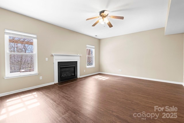 unfurnished living room featuring a glass covered fireplace, wood finished floors, baseboards, and ceiling fan