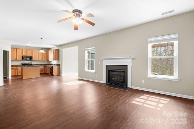 unfurnished living room with visible vents, a glass covered fireplace, dark wood finished floors, baseboards, and ceiling fan