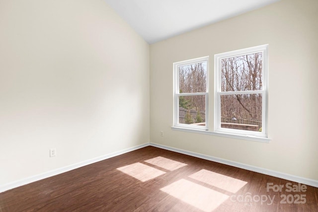 spare room featuring dark wood-type flooring, baseboards, and vaulted ceiling