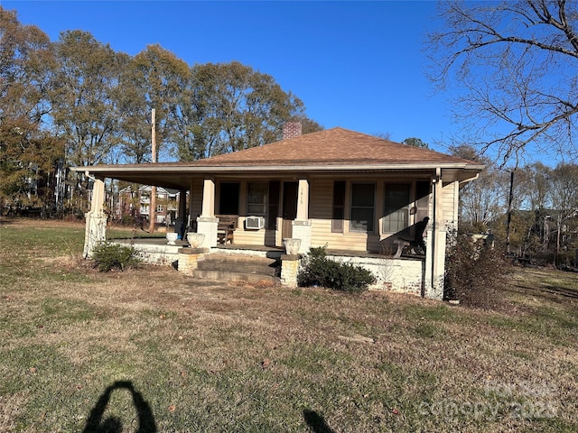 view of front of home featuring a front lawn, cooling unit, roof with shingles, covered porch, and a chimney