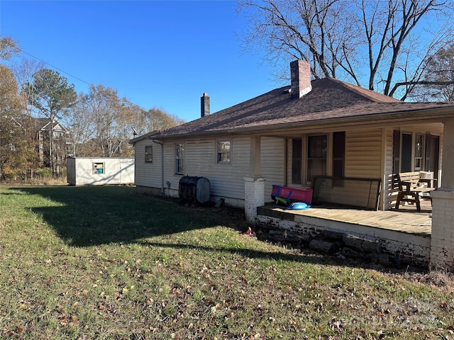 rear view of property featuring a storage unit, a porch, a yard, an outdoor structure, and a chimney