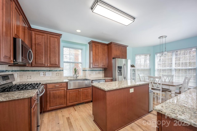 kitchen featuring brown cabinets, a sink, tasteful backsplash, appliances with stainless steel finishes, and light wood finished floors