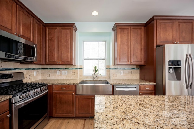kitchen with a sink, light stone countertops, tasteful backsplash, and stainless steel appliances