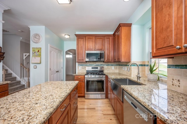 kitchen with backsplash, stainless steel appliances, light wood-style floors, brown cabinetry, and light stone countertops