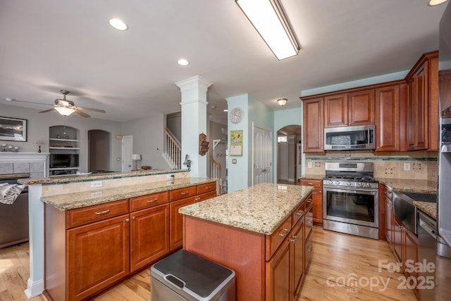 kitchen featuring a ceiling fan, a center island, arched walkways, light wood-style floors, and appliances with stainless steel finishes