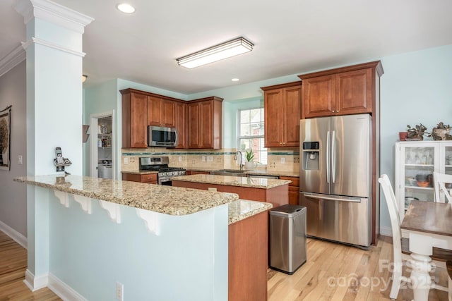 kitchen with backsplash, light stone counters, appliances with stainless steel finishes, a peninsula, and a sink