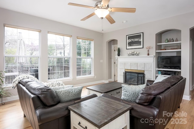living area featuring a ceiling fan, built in features, arched walkways, light wood-style floors, and a fireplace