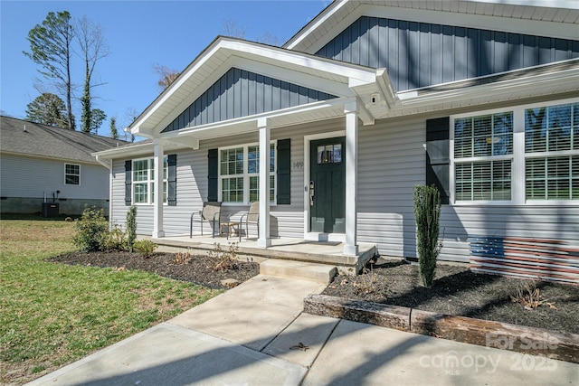 view of exterior entry with a porch, central air condition unit, a yard, and board and batten siding